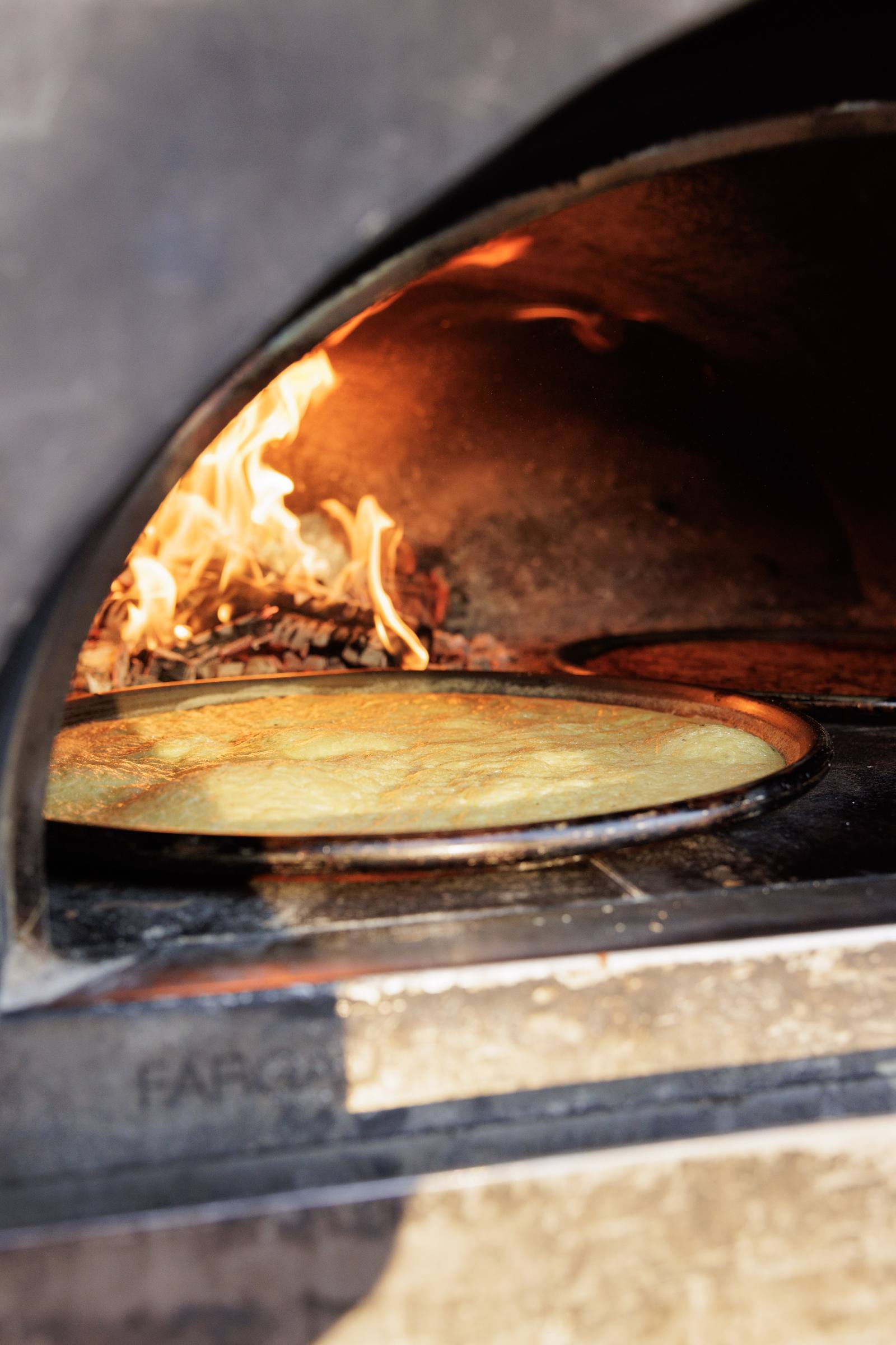 Une socca cuisant dans un four à bois, flammes vives