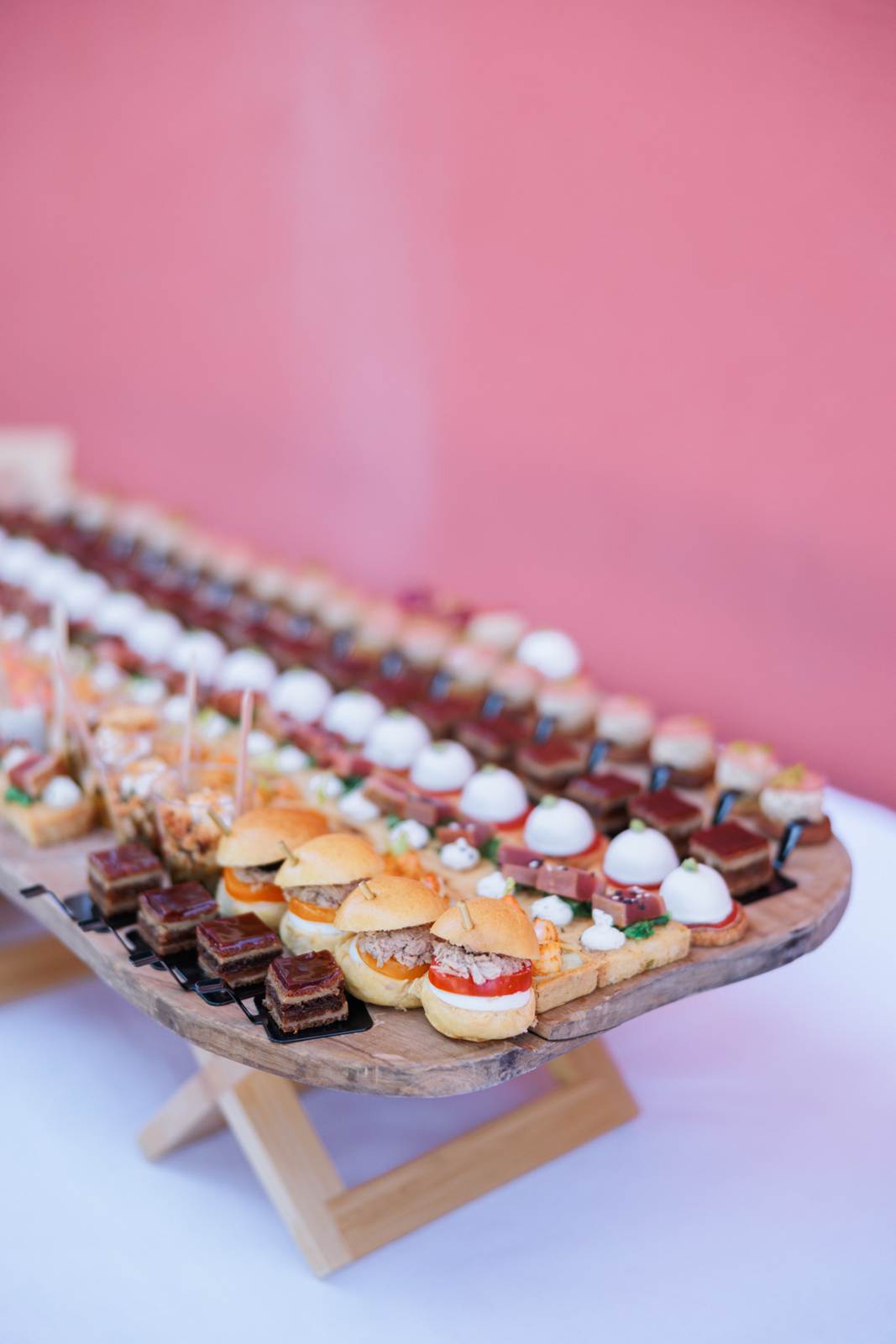 A long wooden board of petits fours and mini burgers